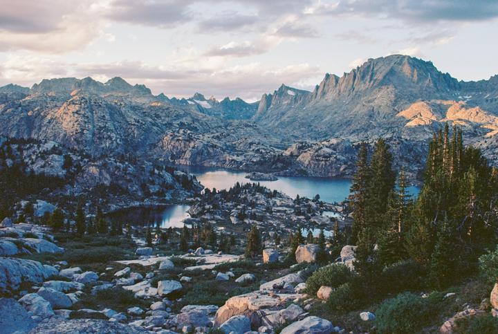 A landscape view shows a rocky mountain range with several lakes and evergreen trees.