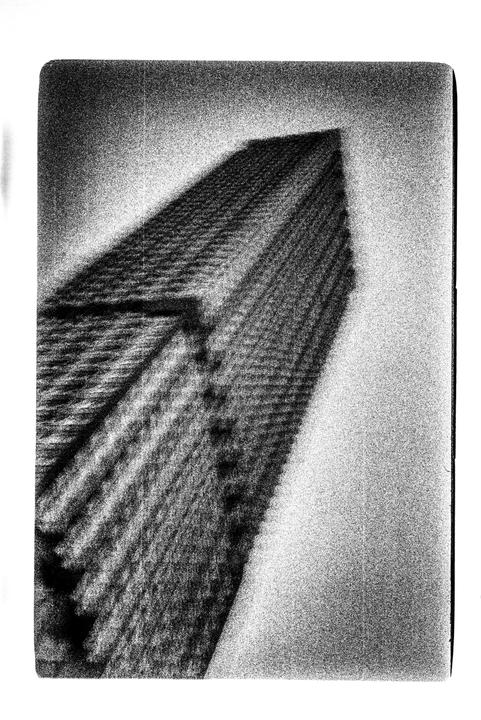 A tall building with a textured facade is angled against a bright sky.