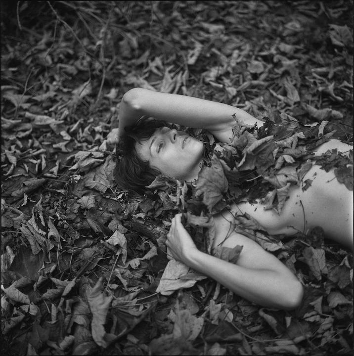 A woman lies on her back covered in autumn leaves.