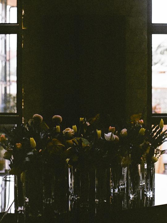 A row of flower arrangements in glass vases sits in front of a window.