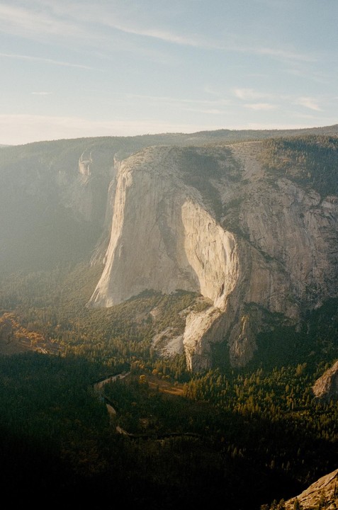 A winding river flows through a valley surrounded by towering cliffs and a dense forest.