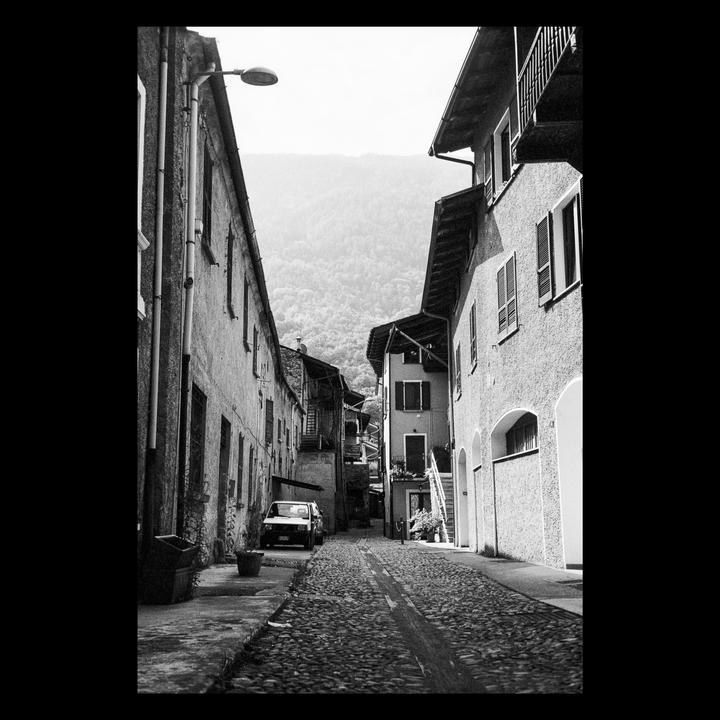 A narrow cobblestone street with buildings on both sides leads to a mountain in the distance.