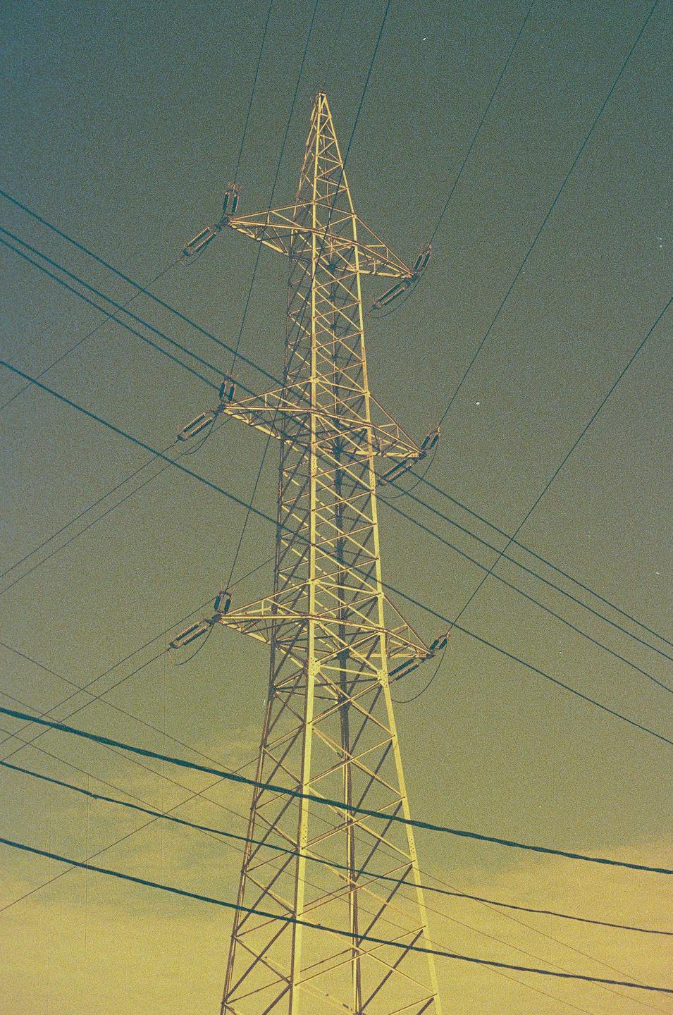 A tall metal electricity pylon stands against a hazy sky with numerous power lines stretching across the frame.
