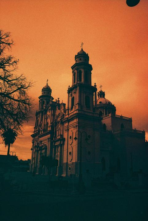 A large, ornate church with multiple towers and domes stands silhouetted against an orange sky.