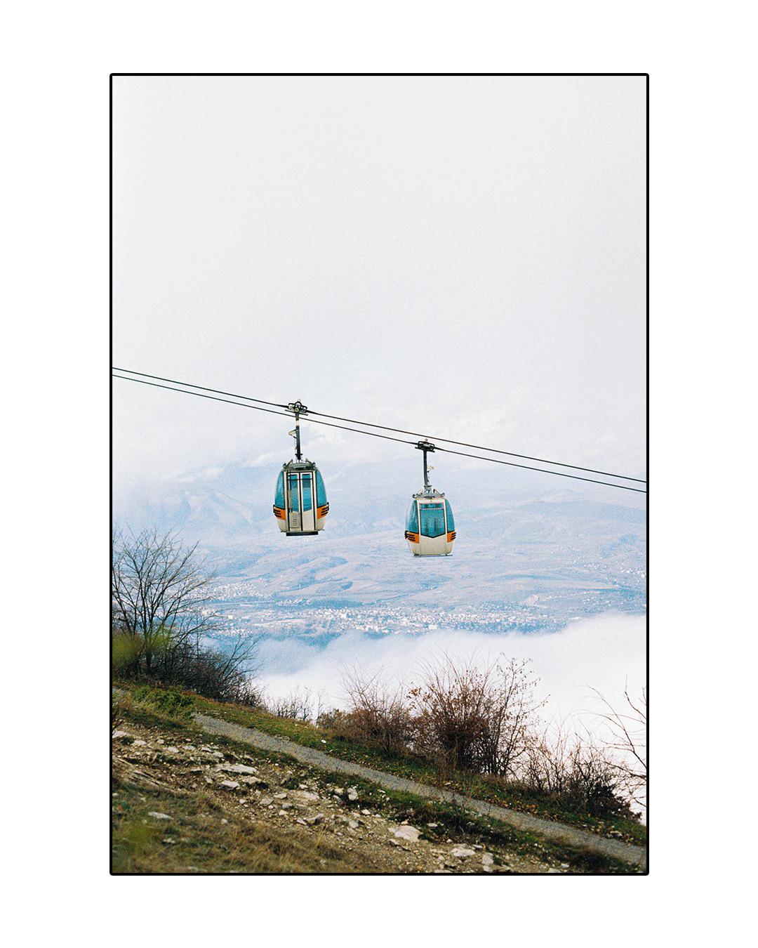Two cable cars are suspended over a valley with a town partially obscured by clouds.