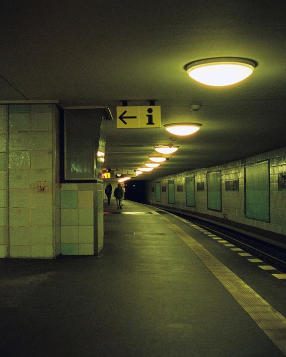 Two people walk along a subway platform illuminated by overhead lights.