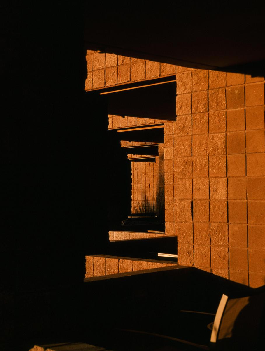 Sunlight illuminates a textured wall and a series of receding architectural elements, creating strong shadows.