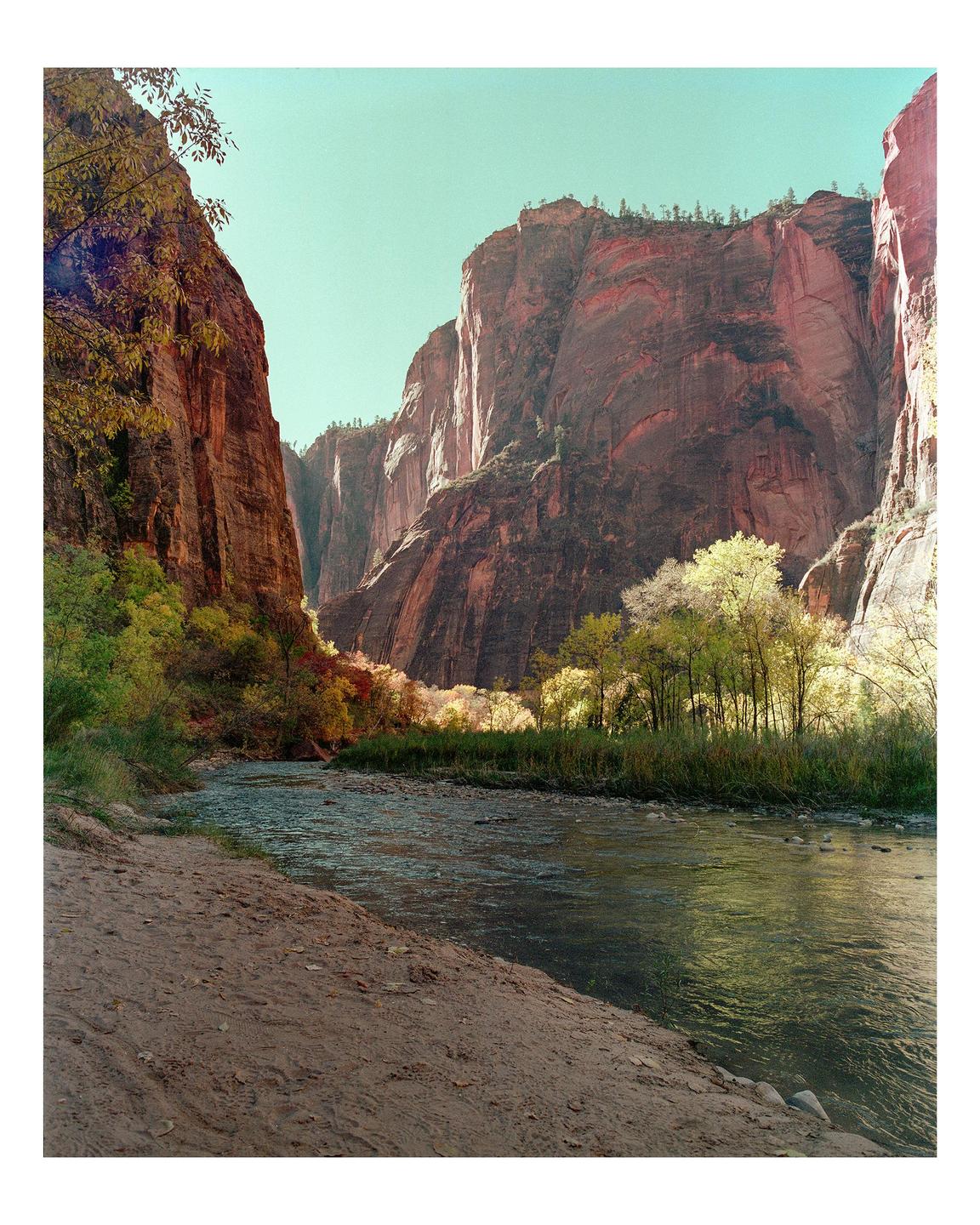 A river flows through a canyon with tall rock walls and trees with autumn foliage.
