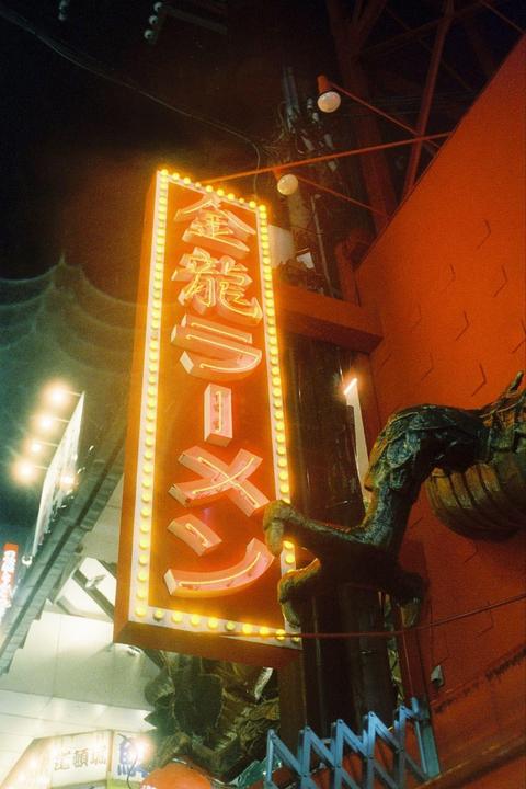A neon sign for a ramen shop illuminates a street at night.