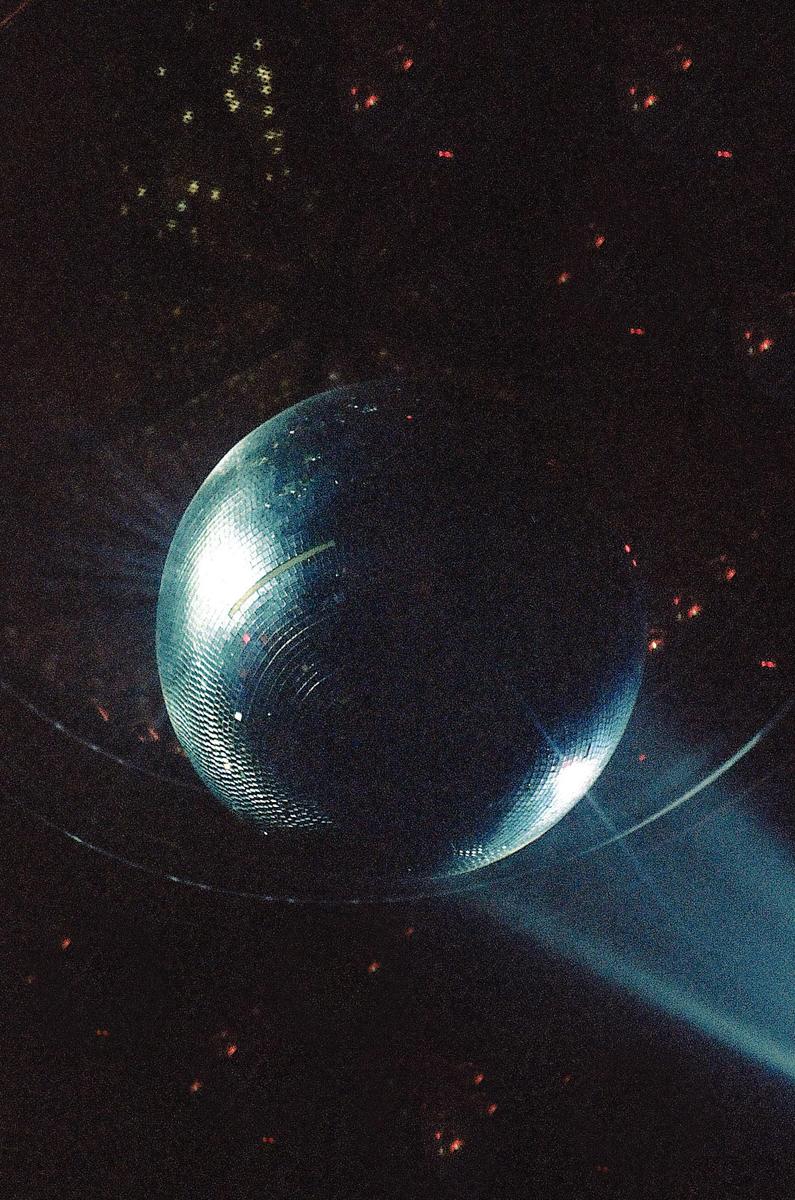 A disco ball reflects light in a dark room, casting small bright spots on the ceiling.