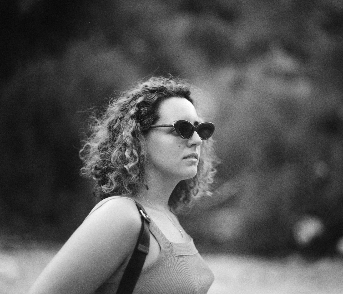 A woman with curly hair and sunglasses looks to the right of the frame.