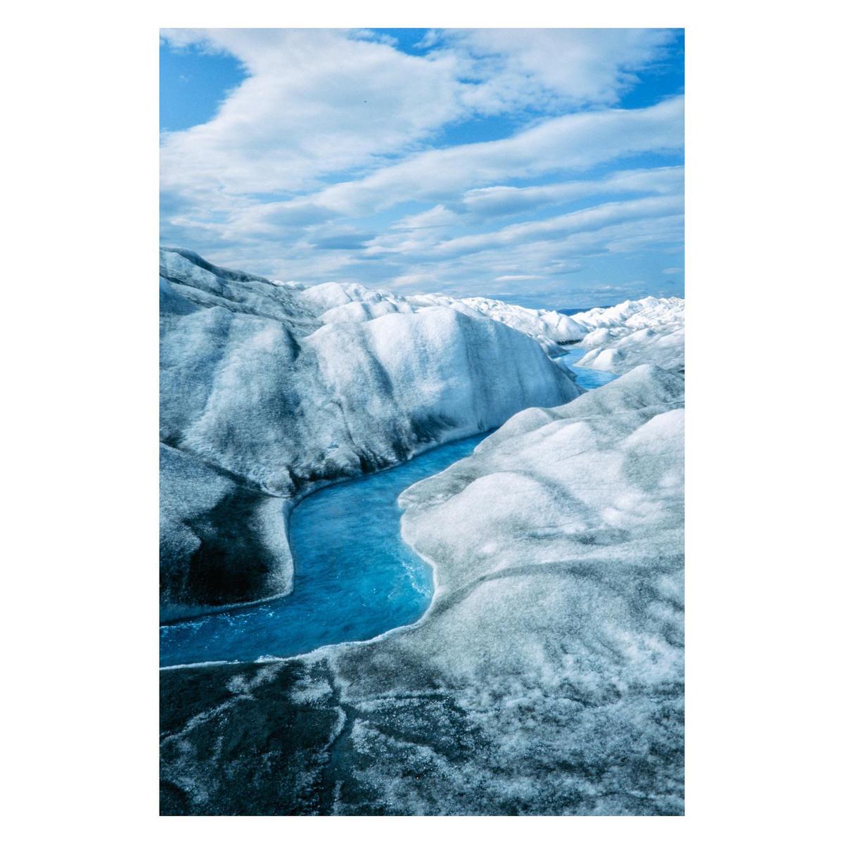 A river of bright blue water flows through a landscape of ice and snow under a cloudy sky.