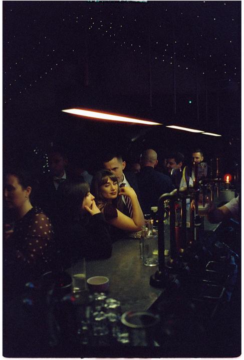 A group of people are gathered around a bar in a dimly lit room with a starry ceiling.
