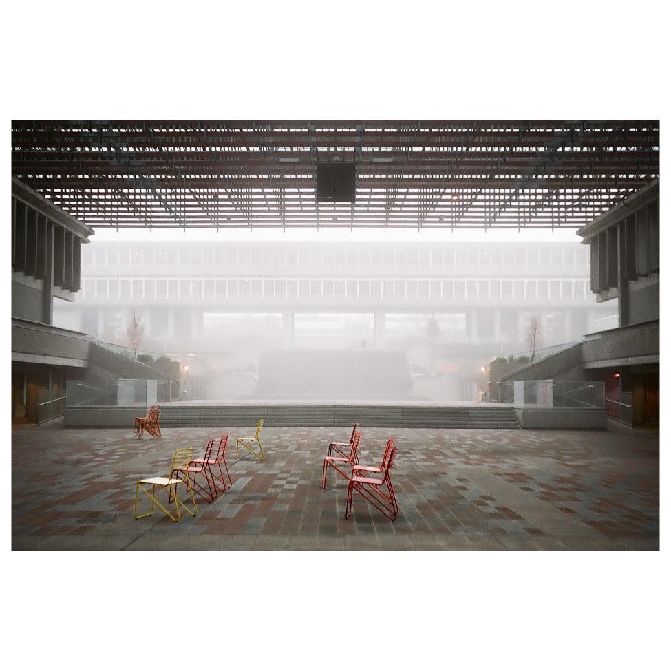 A courtyard with several colorful chairs is visible through a thick fog.