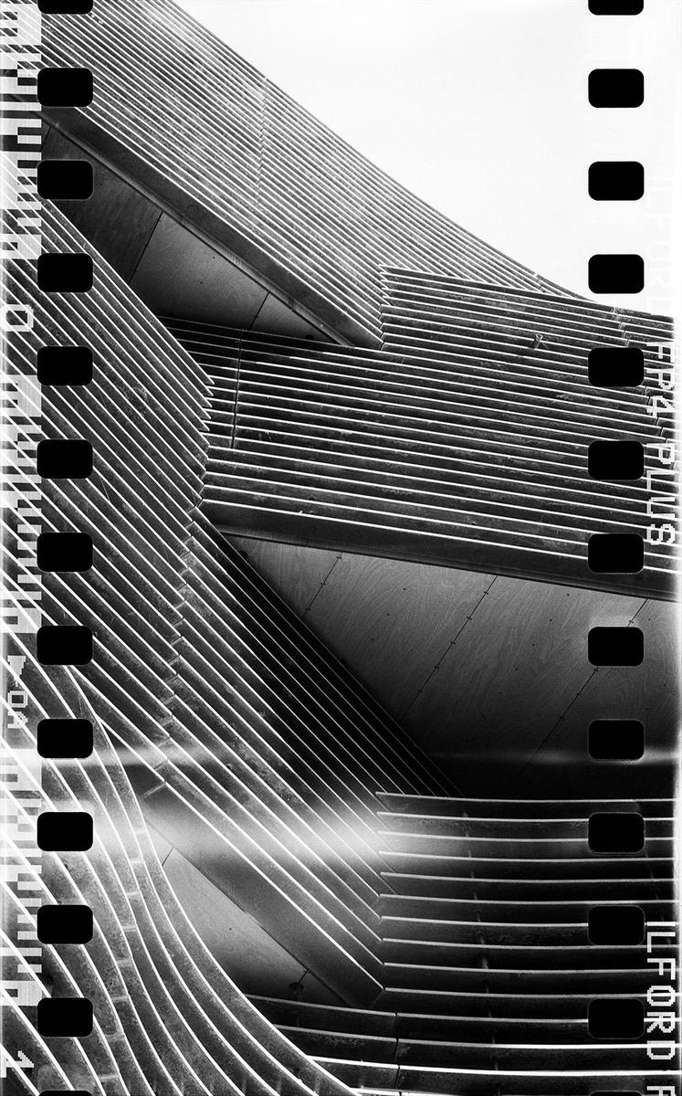 A modern building with horizontal lines and curves is shown in black and white.