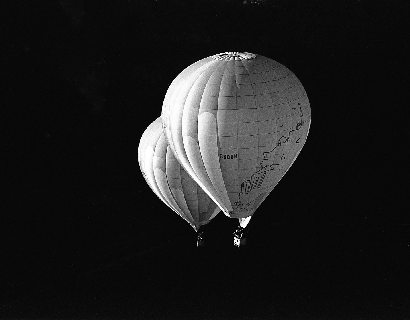 Two hot air balloons with baskets are visible against a dark sky.