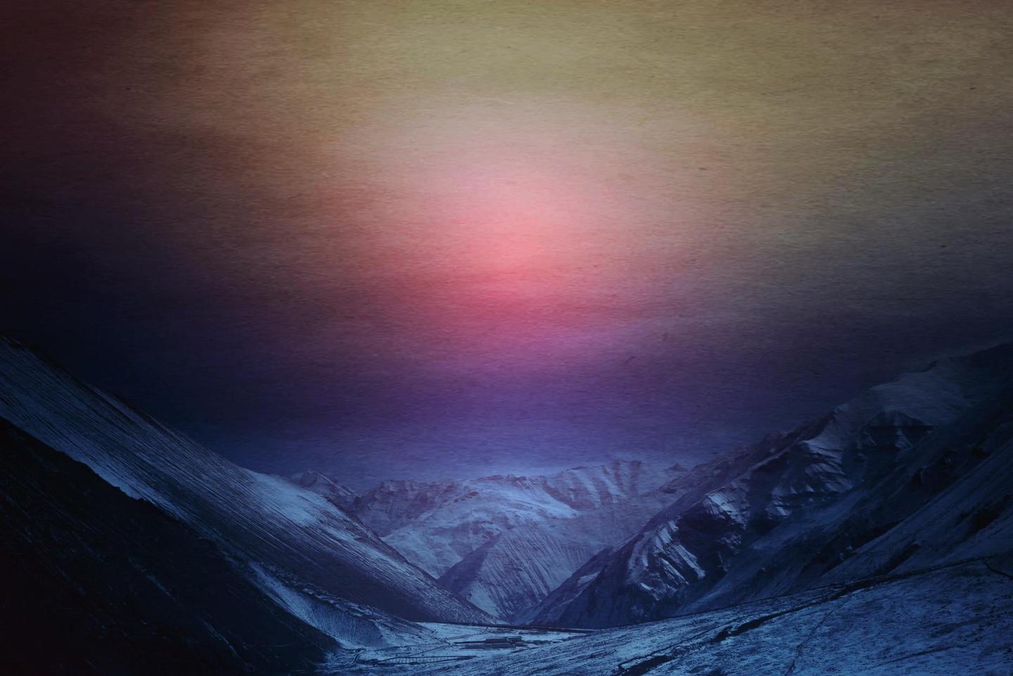 A valley with snow-covered mountains is visible under a colorful sky.