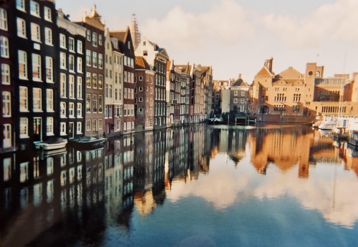 A canal in Amsterdam is lined with historic buildings and their reflections are visible in the water.
