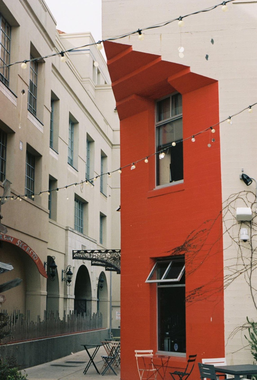 A red building with string lights and outdoor seating is visible next to a beige building with arched entrances.