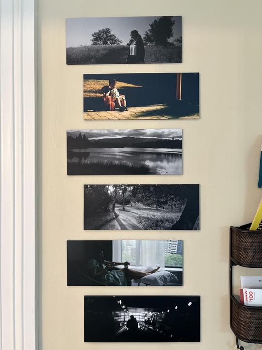 Six rectangular photographs are displayed vertically on a light-colored wall next to a white door frame.
