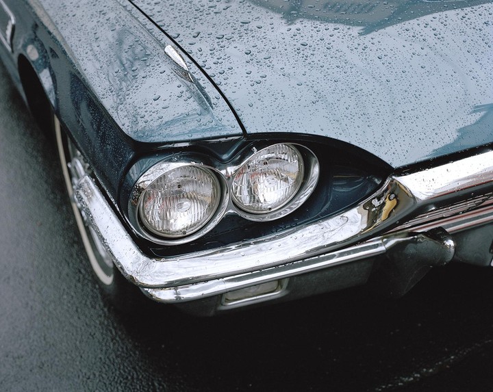 The front of a teal vintage car is covered in raindrops.