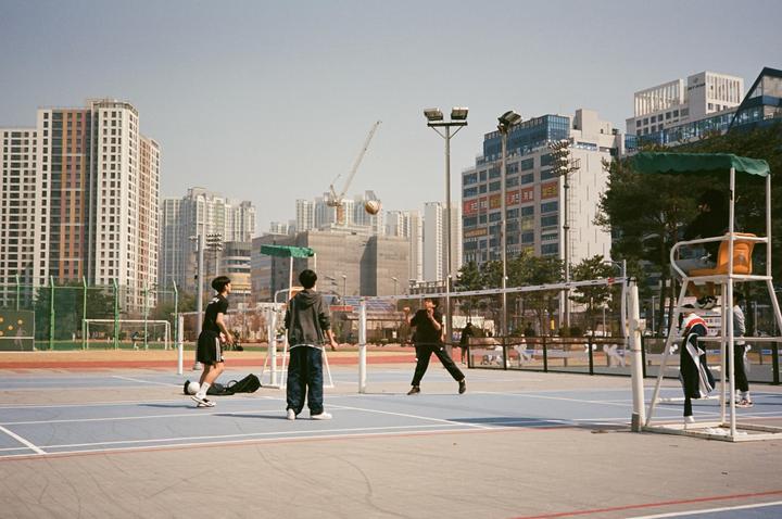 Several men play volleyball on an outdoor court surrounded by tall buildings.