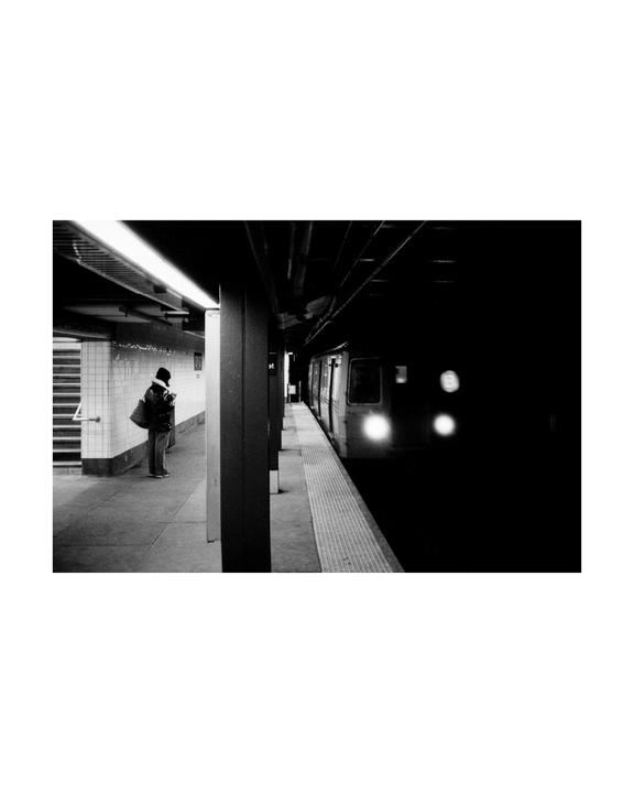 A person stands on a subway platform as a train approaches in the dark.
