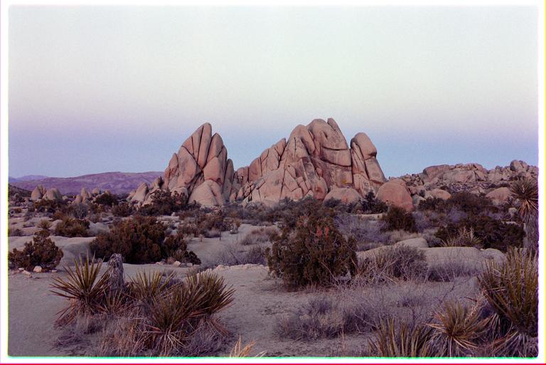 A desert landscape features large rock formations and sparse vegetation under a pale sky.