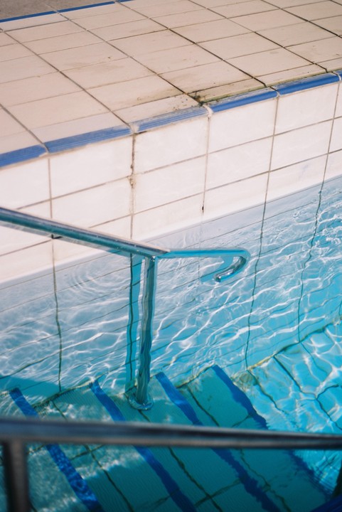 A metal handrail extends into the clear blue water of a swimming pool with tiled edges.