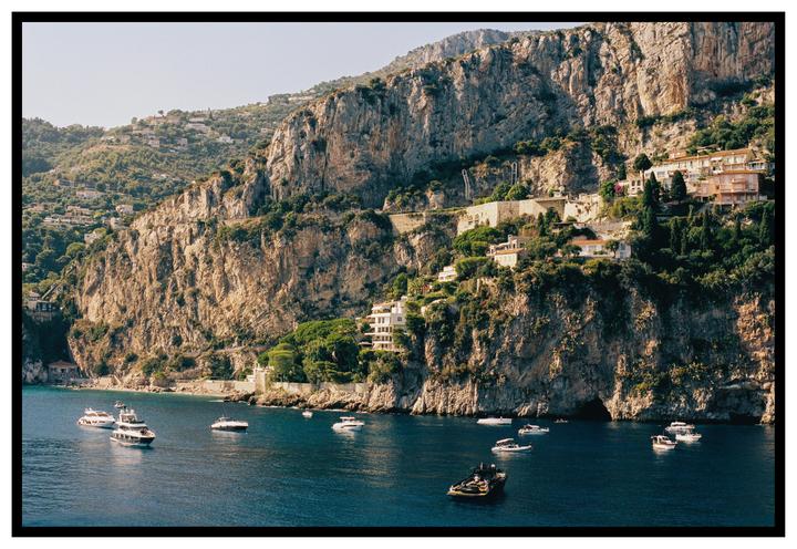 Boats are visible in the water below a cliffside with buildings and trees.