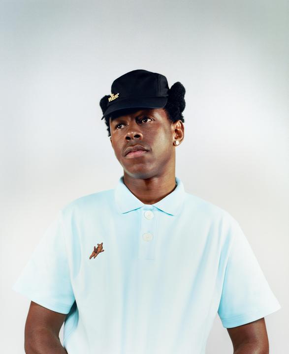 A man wearing a light blue polo shirt and a black cap with ear flaps looks to the side.