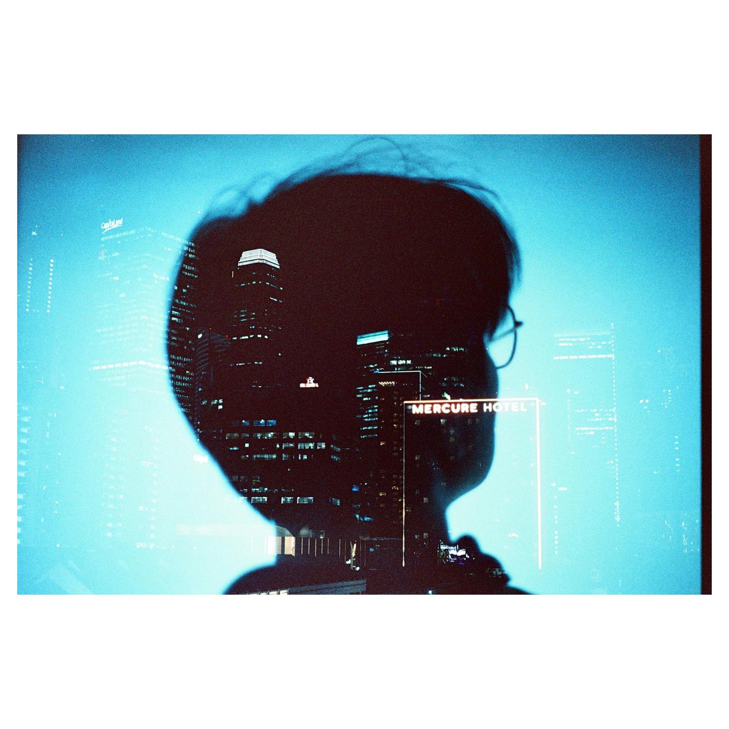 A double exposure shows a silhouette of a person with glasses overlaid with a cityscape at night.
