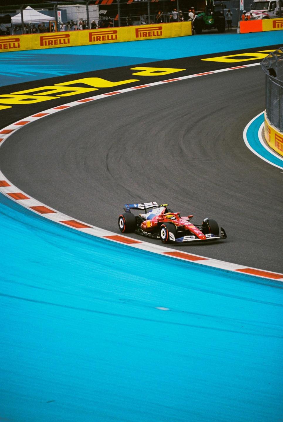 A red and blue race car is speeding around a turn on a race track with yellow and blue markings.