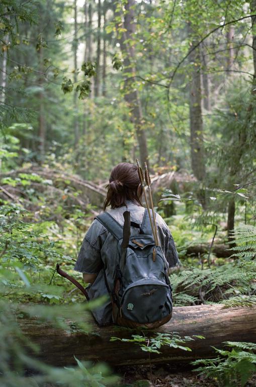 A person with a backpack and arrows sits on a log in a forest.