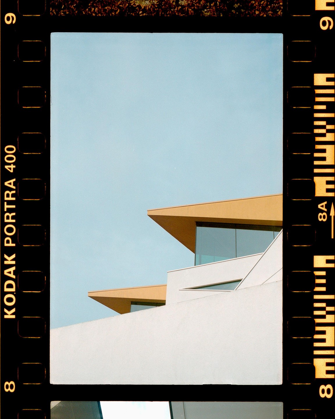 A modern building with angular roofs and large windows stands against a clear sky.