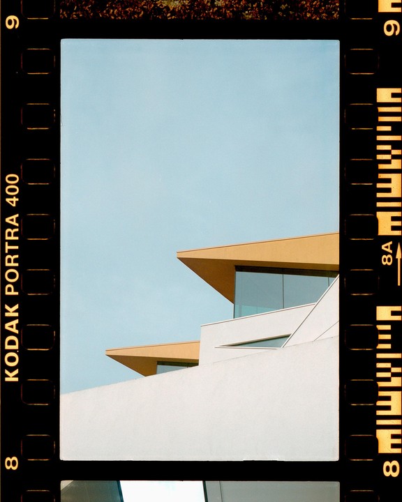 A modern building with angular roofs and large windows stands against a clear sky.