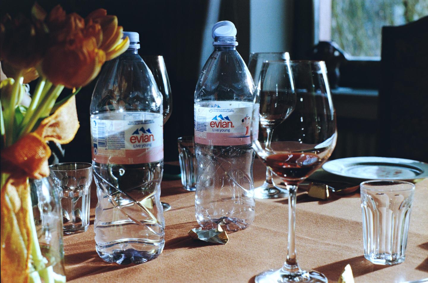 Two plastic bottles of Evian water and several glasses are arranged on a table with a vase of flowers.