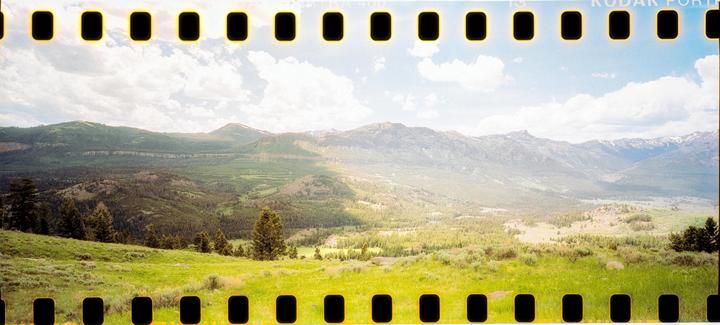 A vast mountain landscape with green hills and valleys under a partly cloudy sky is visible.