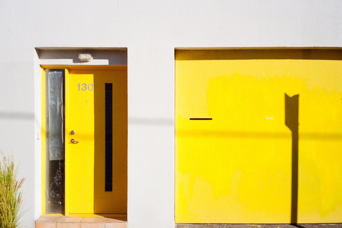 A bright yellow door with the number 130 and a yellow garage door are set into a white wall.