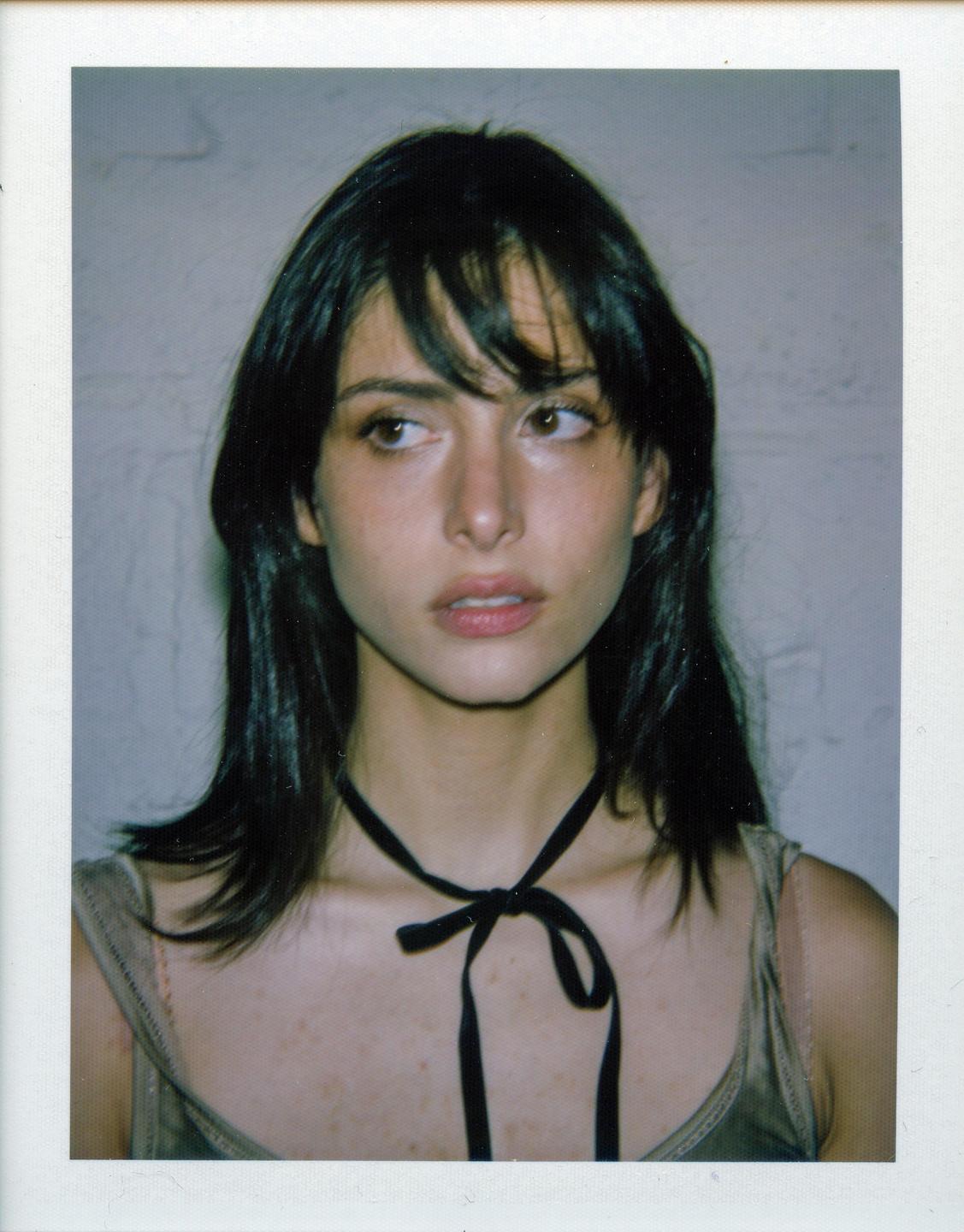 A woman with dark hair and a black ribbon around her neck looks to the right.