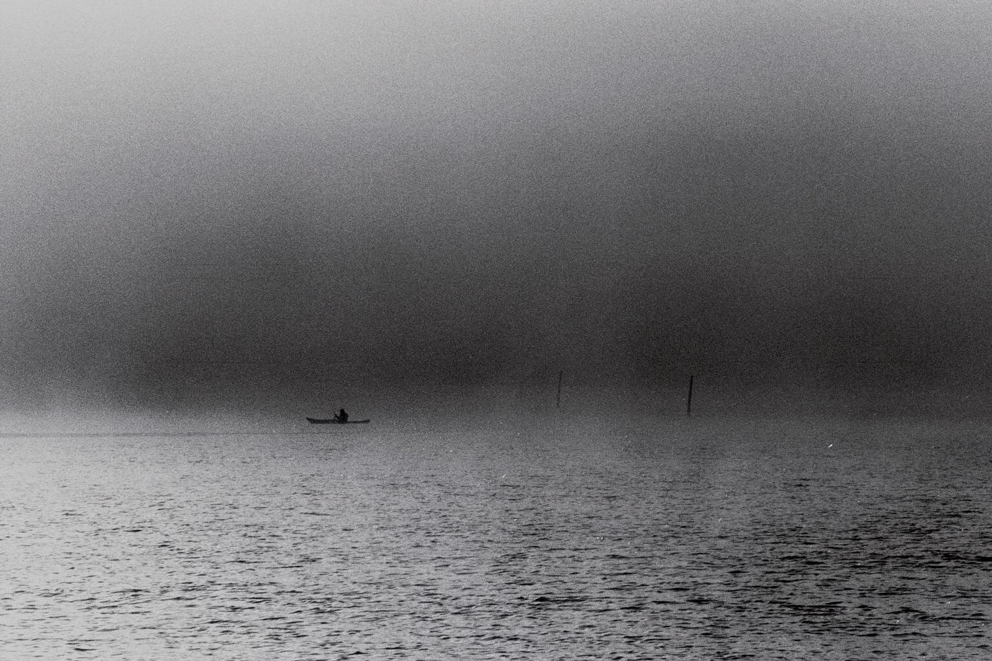 A person in a kayak is on the water in the fog.