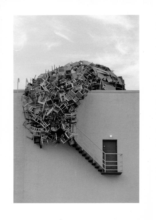 A large pile of chairs is attached to the side of a building above a staircase and door.