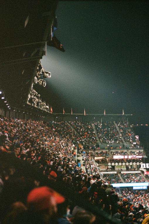 A large crowd of people sits in a stadium at night, illuminated by a spotlight.