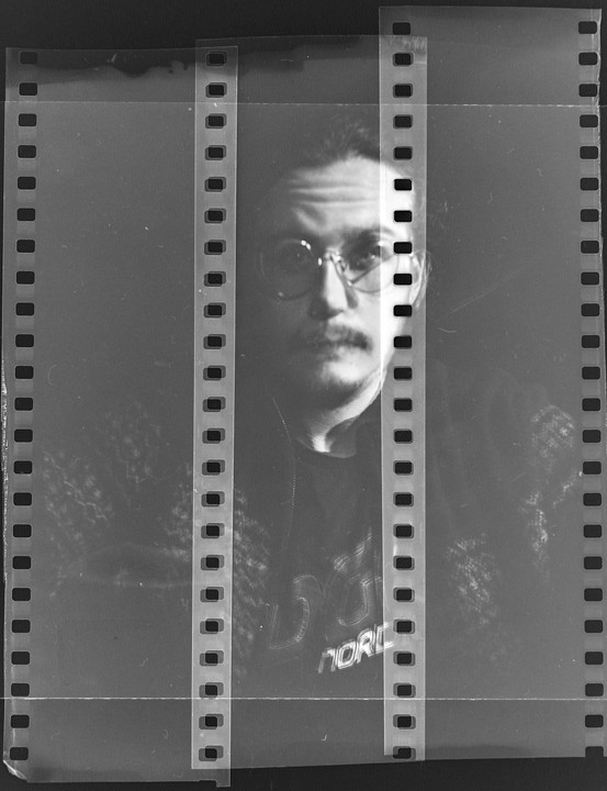 A man with glasses and a mustache is visible through a film negative.