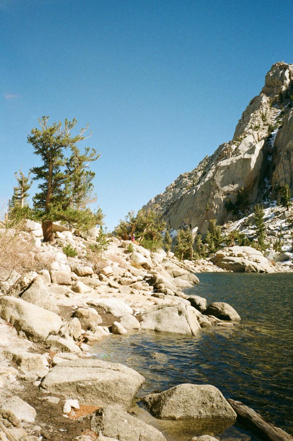 A rocky mountain landscape with a lake and pine trees is visible under a clear sky.
