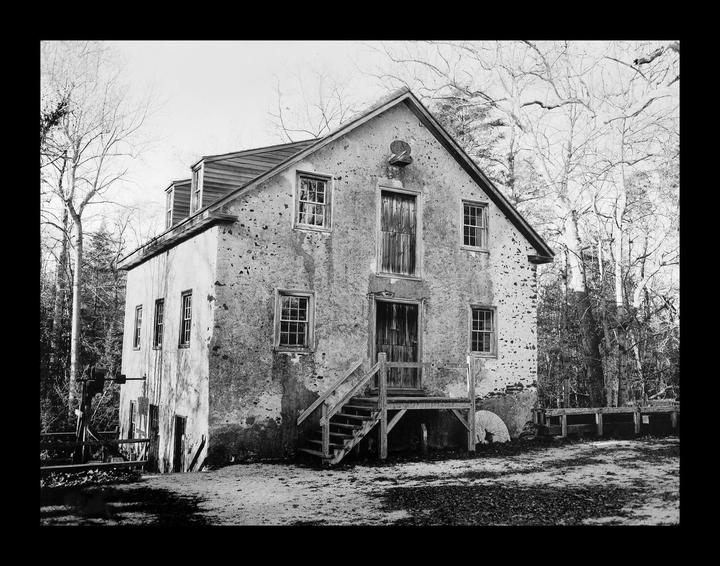 A large, old, stone building with a wooden staircase leading to its entrance stands among bare trees.
