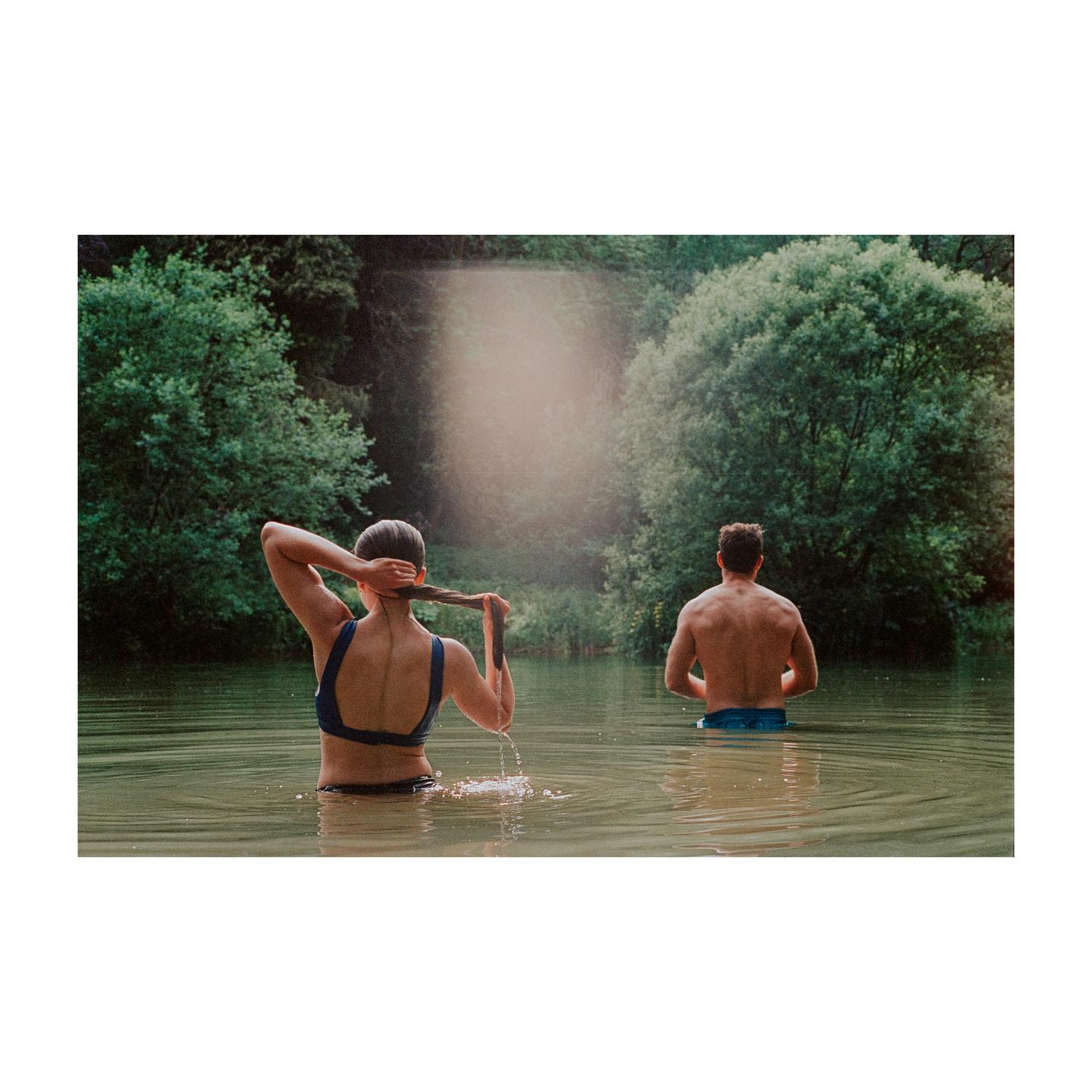 A woman and a man are standing in a body of water surrounded by trees.