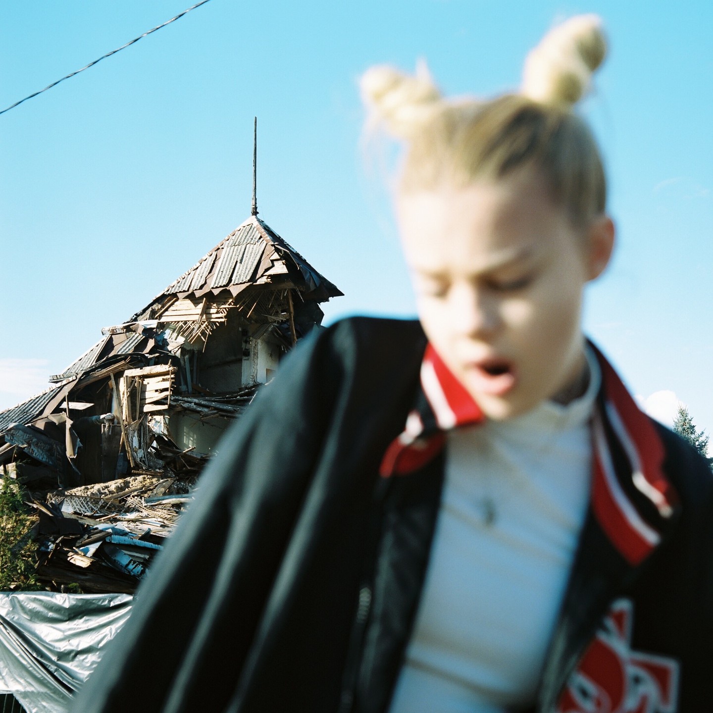 A blurry girl with her mouth open stands in front of a dilapidated building under a clear sky.