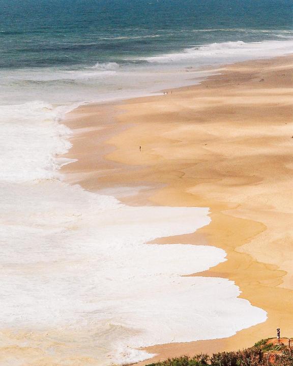Waves crash on a sandy beach with a few people walking in the distance.