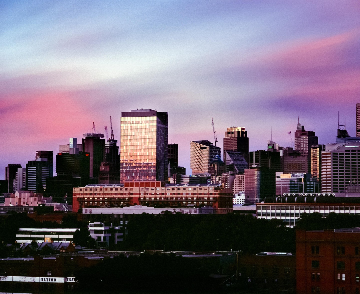 A cityscape with many buildings is visible under a colorful sky at dusk.